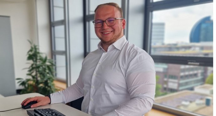 © Mainova Junger Mann mit weißem Hemd und Brille steht im Büro