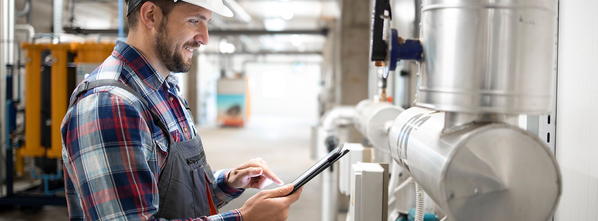 © istockphoto.com/Smederevac Installateur im Heizungraum steht an den Leitungen und prüft mit dem Tablet die Werte