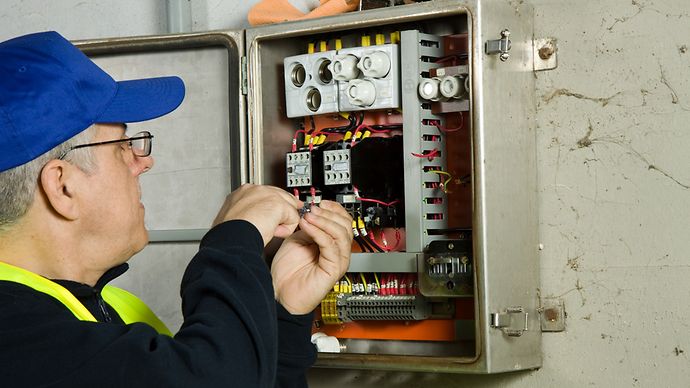 Älterer Herr arbeitet an einem Schaltschrank.